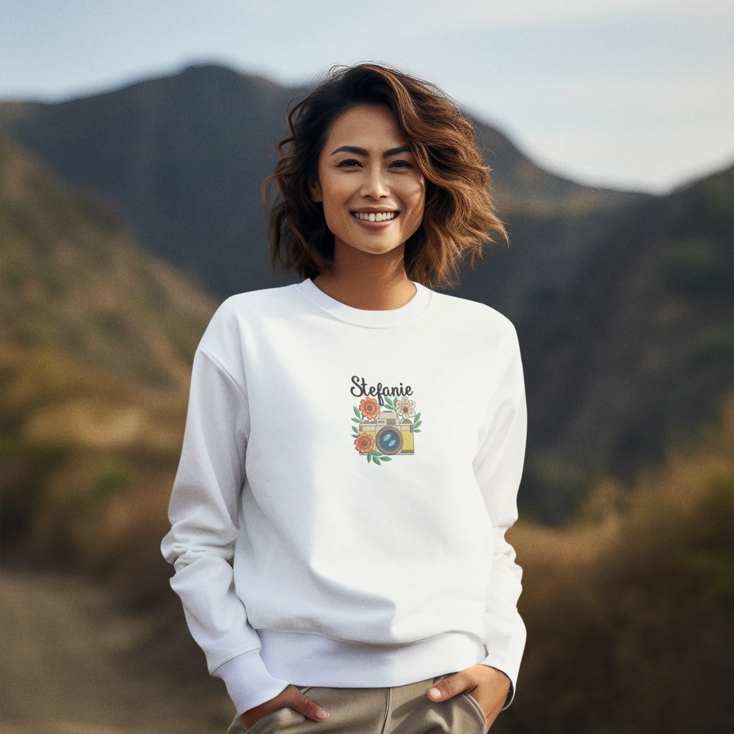 Frau trägt ein weißes Sweatshirt mit besticktem Kamera- und Blumenmotiv sowie personalisiertem Namen Stefanie.